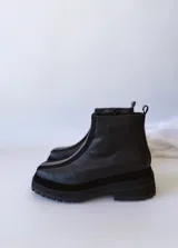 Botas negras de cuero con caña baja, cierre lateral con cremallera y suela track.