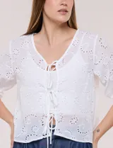 Cardigan corto de broderie blanco con escote en V y cierre frontal de lazos para anudar. Presenta mangas tres cuartos abullonadas con puño elástico y diseño perforado con motivos florales.