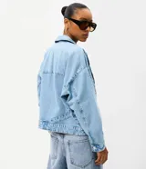Campera de jean oversized de corte amplio con recortes estructurales, cierre frontal con botones metálicos, cuello clásico y bolsillos frontales.