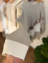 Buzo de tejido de punto con diseño oversize y calce relajado. Presenta un diseño de bloques de color en tonos neutros con una franja diagonal central en material metalizado brillante. Cuenta con cuello redondo y mangas largas con puños acanalados.