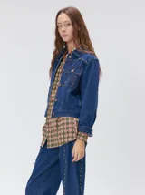 Campera denim crop de mezclilla oscura, con apliques metálicos en el pecho, bolsillos delanteros cruzados con detalles bordados y de parches.