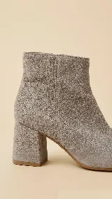 Botas de caña alta desmontables de gamuza color beige, con taco cuadrado de 6 cm y punta semi cuadrada. Presentan un diseño con costura central y detalle de estribo con hebilla forrada en el tobillo.