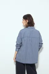 Camisa de silueta amplia y caída fluida, color celeste con rayas verticales blancas. Presenta cuello camisero clásico, cierre frontal con botones y un bolsillo aplicado en el pecho. Las costuras están resaltadas en azul oscuro.