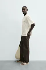 Camiseta de corte relaxed fit, color blanco roto, con cuello redondo y manga corta. Presenta un pequeño estampado en el pecho con un dibujo lineal y texto.