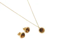 Set de joyería compuesto por un collar y un par de aros tipo caravanas, confeccionados en acero con baño de oro. Ambas piezas presentan un diseño circular con borde trenzado y una piedra central de ojo de tigre.