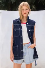 Chaleco de jean negro, con cuello camisero, cierre frontal de botones, dos bolsillos con solapa en el pecho y dos bolsillos de parche en la parte inferior. Incluye tiras ajustables en los laterales.