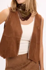 Chaleco de gamuza sintética color marrón, con costuras artesanales en contraste a lo largo de los bordes frontales y diseño sin mangas.