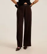 Pantalón recto color marrón chocolate, confeccionado en crepé, con trabillas en la cintura, cinturón con hebilla y pliegues.