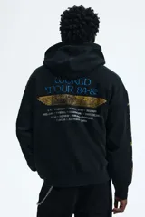 Canguro negro de corte oversized con capucha, bolsillo frontal tipo canguro y estampado frontal de la banda Iron Maiden con diseño de momia. Las mangas presentan detalles estampados en color dorado con motivos egipcios.