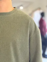 Buzo oversize de tejido waffle en color beige, con cuello redondo y manga larga, con pequeña etiqueta de marca en el dobladillo inferior.