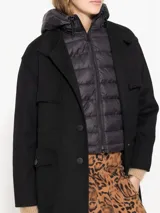 Tapado negro de paño con chaleco interno desmontable con cierre en el cuello. Tiene acceso mediante botones y bolsillos plaque en el delantero.