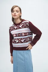 Buzo tejido de punto con diseño jacquard que presenta motivos de corazones, flores y aves en tonos bordó, blanco y celeste. Posee cuello redondo, puños y ruedo acanalados.