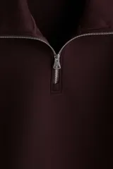 Buzo bordó de tejido pesado con efecto neopreno, cuello elevado y medio cierre metálico. Cuenta con hombros caídos, mangas largas y puños y bajo acanalados.