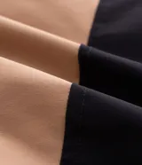 Chaqueta tipo parka de poliéster con diseño en bloques de color negro y tostado. Presenta capucha ajustable con cordones, cierre frontal con solapa superpuesta y bolsillos frontales con tapa.
