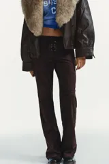 Pantalón de tiro bajo confeccionado en gamuza marrón, con diseño flare y detalle de lazada frontal. Presenta costuras marcadas y cierre lateral con cremallera.