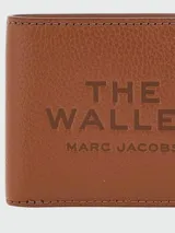 Billetera Marc Jacobs modelo The Billfold, color negro, con diseño plegable de cuero texturizado y estampado frontal en relieve con el texto "The Wallet" y la marca.