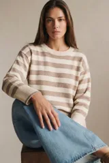 Sweater de punto con diseño a rayas horizontales en color negro y crema. Presenta cuello redondo, mangas largas con puños acanalados y un detalle de borde en tono bronce metalizado en el ruedo y los puños.