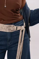 Faja de cuero gamuzado metalizado color visón, con curvatura anatómica, herraje metálico plateado y tiras largas con flecos para atar en nudo.