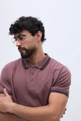 Polo de piqué de manga corta color malva, con cuello y puños tejidos a contratono en azul marino. Lleva cartera de tres botones y logo bordado en el pecho.