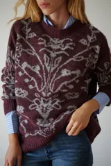 Buzo de tejido de punto en color marrón con un patrón ornamental floral en color celeste. Presenta cuello redondo, mangas largas y un corte holgado.