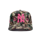Gorro trucker con estampado de camuflaje de bosque, visera curva y cierre trasero ajustable. Presenta un aplique bordado en relieve con las letras "NY" en color fucsia en el centro, acompañado de los textos bordados "Mi Casa" y "Su Casa" a los lados.