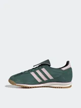 Zapatillas Adidas modelo SL 72 OG LT, de diseño retro inspirado en el running y el fútbol. Presentan un cuerpo de gamuza en color verde oscuro con las icónicas tres tiras laterales en tono rosado claro. Incluyen una lengüeta larga distintiva, entresuela blanca con detalles en rosa y suela de goma dentada color caramelo.