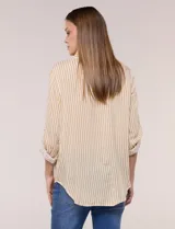 Camisa de corte clásico y silueta relajada con diseño de rayas verticales en blanco y negro. Presenta cuello camisero tradicional, cartera frontal con botones, un bolsillo aplicado en el pecho con rayas horizontales y mangas largas con sistema para arremangar.