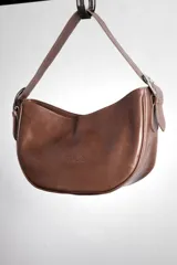 Cartera tipo lady bag color lila, de cuero sintético, con correa ajustable y herrajes metálicos plateados.