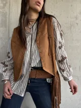 Chaleco de gamuza color camel forrado, con ribetes decorados con tachas metálicas y tiras colgantes con flecos en el lateral.
