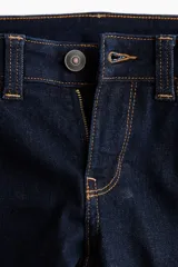 Jean de denim elástico azul oscuro, de tiro bajo, tiro ajustado desde la cintura hasta el muslo y corte acampanado desde la rodilla hacia el bajo. Cuenta con bolsillos delanteros y traseros, cierre frontal con botón y costuras en contraste de color naranja.