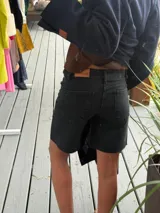 Bermuda de jean negro, tiro medio, con dobladillo deshilachado y botón metálico dorado con logo.