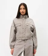 Campera bomber color gris de sarga, con cuello alto, cierre frontal con botones y bolsillos con solapa en el pecho. Presenta mangas largas con puños elásticos y ruedo ajustable con elástico.