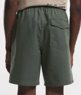 Bermuda masculina color marrón, confeccionada en tejido plano de algodón texturizado con poliéster. Presenta cintura elástica con cordón de ajuste y un tag de marca en el lateral inferior.