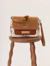 Cartera tipo bandolera con solapa de gamuza color tostado, cuerpo con estampado de piel de serpiente y detalle frontal en cuero texturizado color marrón. Incluye correa ajustable y herrajes metálicos.