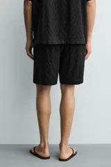Bermuda de corte regular confeccionada en tejido fluido con textura jacquard geométrica. Presenta cintura elástica con cordón ajustable, bolsillos laterales y bolsillos traseros de vivo.