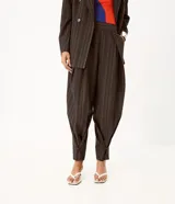 Pantalón de sastre de corte wide leg con diseño de rayas verticales, confeccionado en crepé color gris oscuro. Cuenta con tiro alto, pinzas profundas en el frente y detalle de tira ajustable con botón en el ruedo.