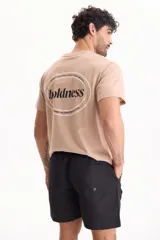 Remera color tostado de manga corta y corte regular fit, con estampa en la espalda dentro de un óvalo con la inscripción "boldness".