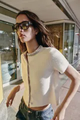 Chaqueta de punto de lana con manga corta, cuello redondo decorado con abalorios joya y cierre frontal con botones forrados a tono.