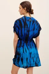 Vestido corto azul con estampado tie-dye en tonos negros y azules, escote en V cruzado, mangas cortas y cordón ajustable en la cintura. Presenta detalles de aplicaciones bordadas con lentejuelas en hombros y falda.