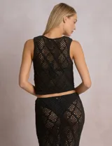 Chaleco negro de tejido calado con patrón geométrico de rombos, corte corto, escote en V pronunciado y cierre frontal con lazos ajustables.