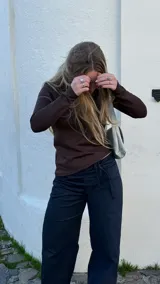 Pantalón de denim oscuro con corte recto y tiro medio. Presenta bolsillos traseros, cierre lateral invisible y tiras ajustables en la cintura.