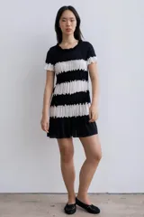 Vestido corto de corte recto con diseño a rayas horizontales en blanco y negro. Presenta franjas plisadas que aportan textura, escote redondo con detalle fruncido y mangas cortas con volados.