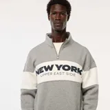 Buzo gris con cuello alto y cremallera parcial, con franja blanca horizontal en el pecho con la inscripción "New York Upper East Side" en azul marino.