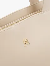 Cartera tipo tote color beige con acabado liso, doble asa superior de cinta y logotipo metálico dorado de la marca en la parte frontal. Cuenta con compartimiento principal con cierre de cremallera.