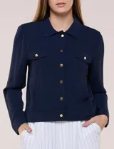 Camperita liviana de corte recto y acabado crepé color blanco, con cuello camisero clásico y cierre frontal de botones metálicos dorados. Presenta bolsillos en el pecho con solapa y mangas largas con puños abotonados.