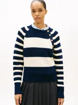 Sweater de punto de algodón con diseño a rayas horizontales en azul marino y blanco, cuello redondo y manga raglán. Cuenta con hilera de botones dorados decorativos sobre el hombro izquierdo.