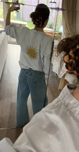 Camisa de corte suelto con estampado de rayas finas, cuello redondo y mangas largas con puños elásticos. Presenta un bordado central en la espalda con diseño de sol en color amarillo.