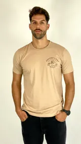 Remera de algodón color beige con cuello redondo y mangas cortas. Presenta un estampado gráfico pequeño en el pecho con la leyenda 'High Spirits Diner' y un dibujo de una calavera.