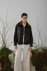 Camisa marrón de cuero sintético con cuello de piel sintética color marrón, cierre frontal con botones a presión dorados, dos bolsillos con solapa en el pecho y corte holgado.