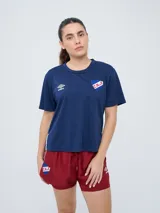 Remera de fútbol Umbro del Club Nacional de Football, modelo Bink para mujer. Diseño azul oscuro con cuello redondo y mangas cortas, con logo de Umbro en el pecho derecho y escudo del club en el pecho izquierdo.